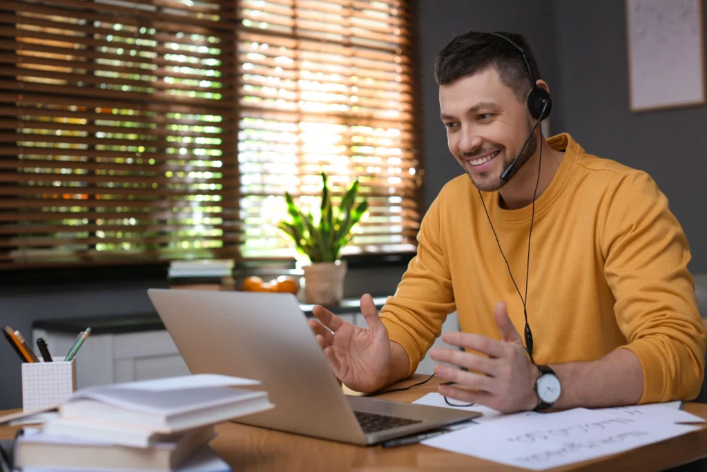 Tutor wearing a headset gesturing while teaching a live online maths lesson through a laptop video call.